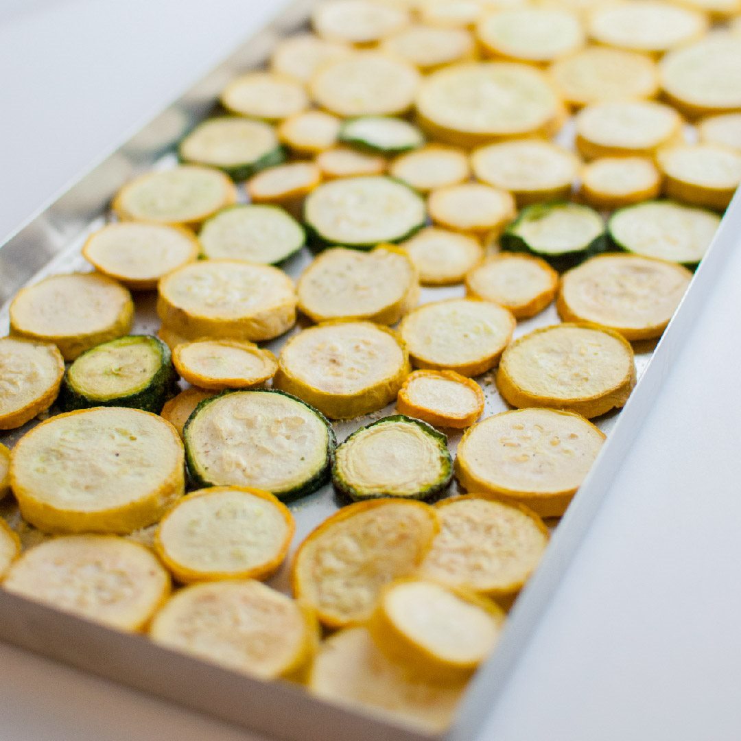 Evenly sliced yellow squash and courgettes arranged on freeze dryer trays